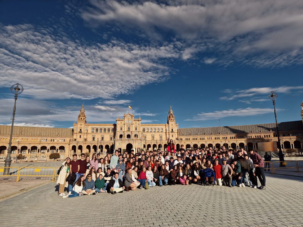 Large group posing in front of a historic building under a blue sky.