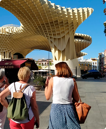 Three people walking toward a large wooden lattice structure, under a clear blue sky.