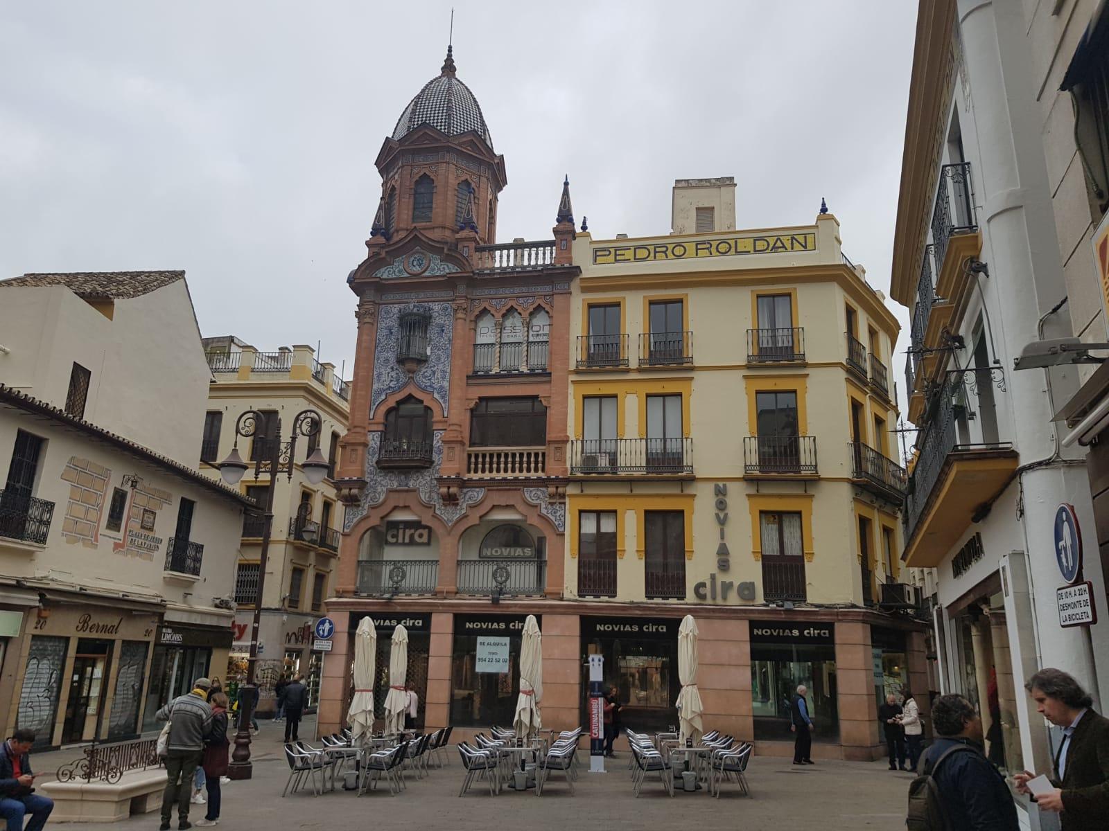 European plaza with ornate buildings, outdoor seating, and pedestrians.