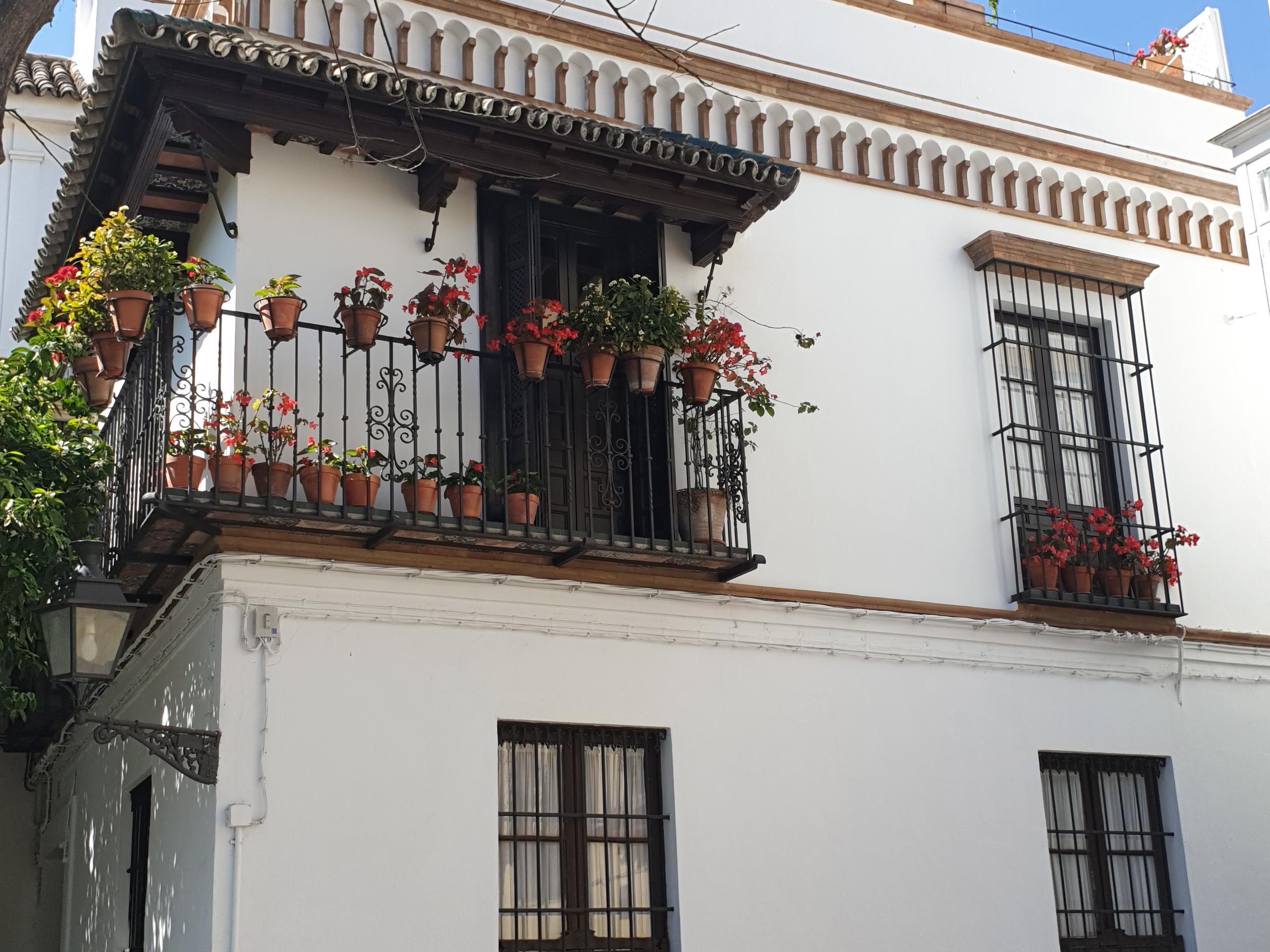 White building with balcony, potted plants, and decorative railings.