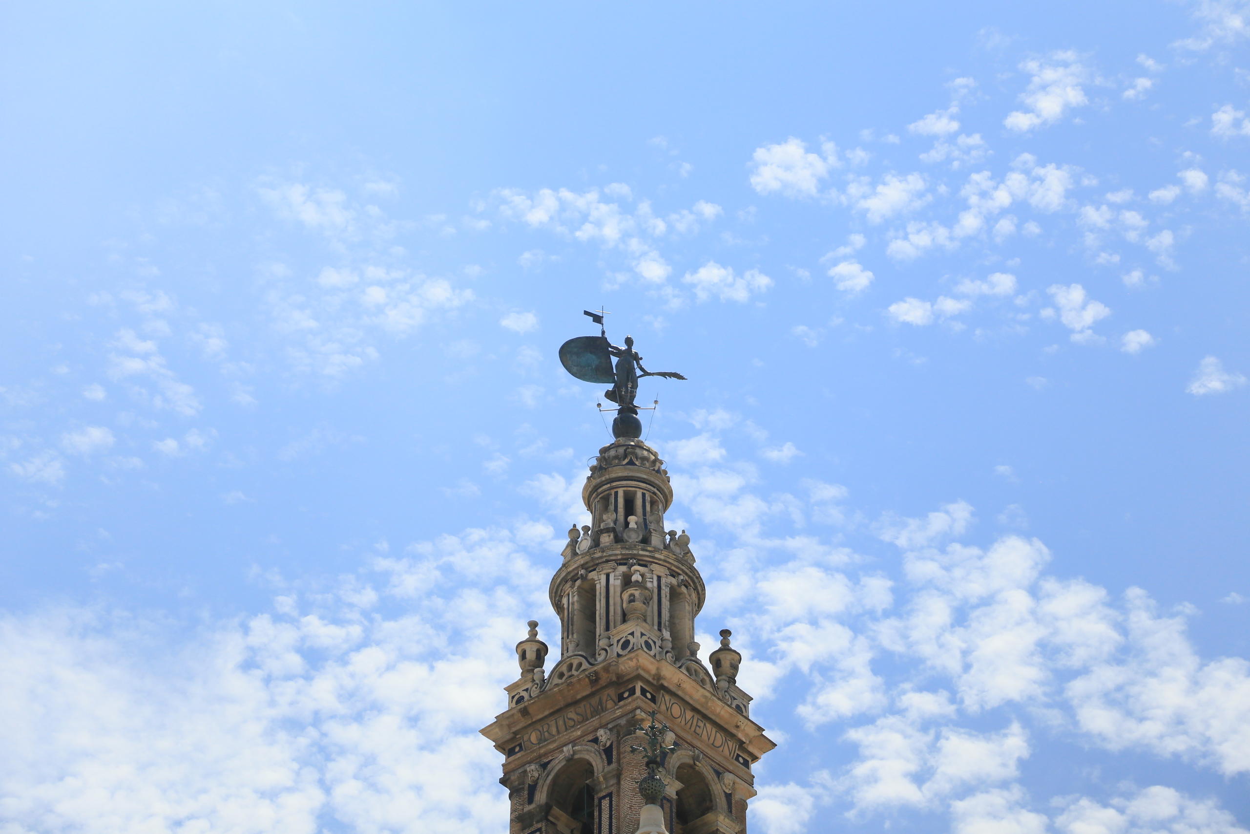 Ornate tower with a weather vane against a blue sky with clouds.