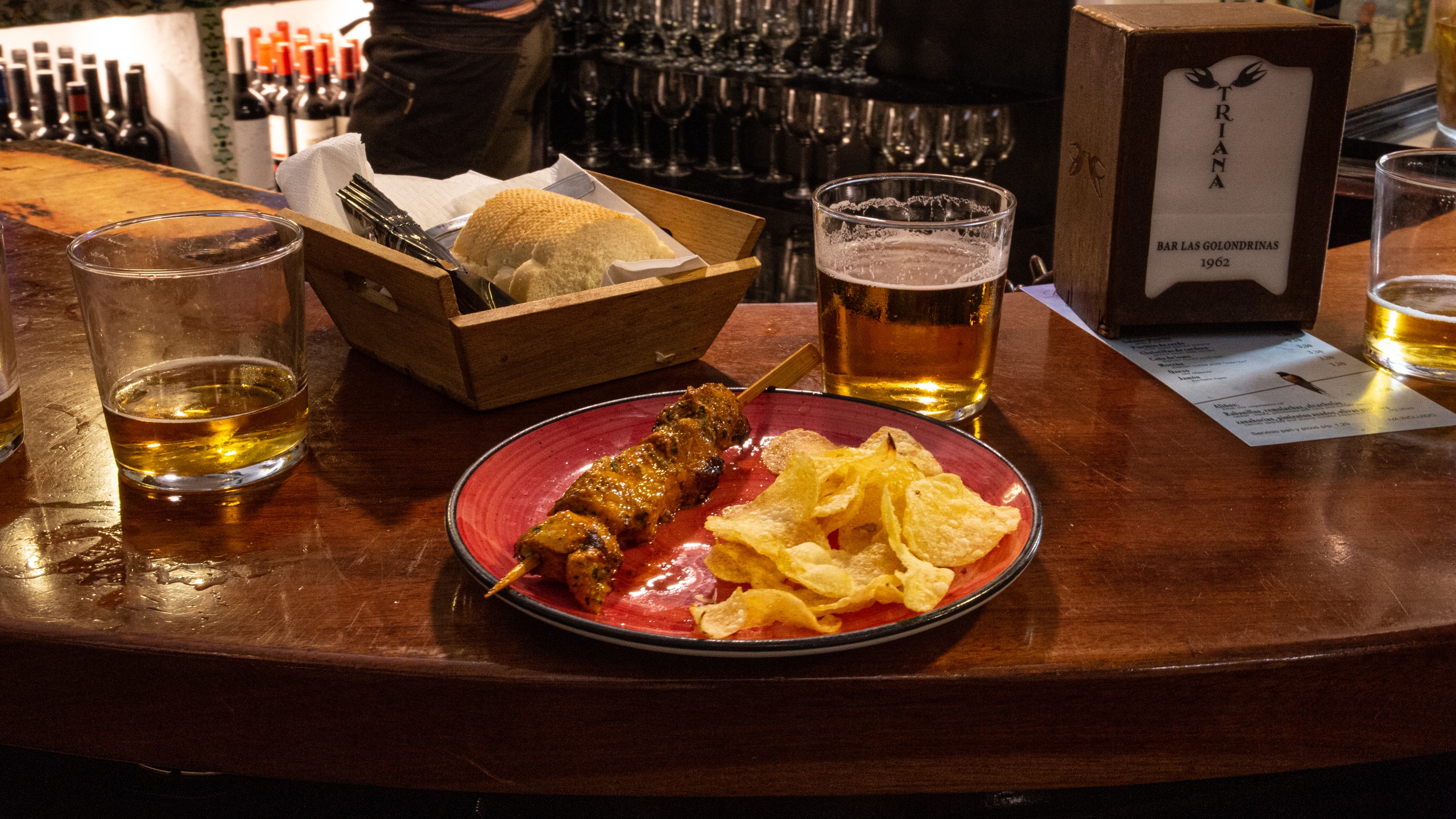 Bar counter with beer, skewers, chips, and a bread basket.