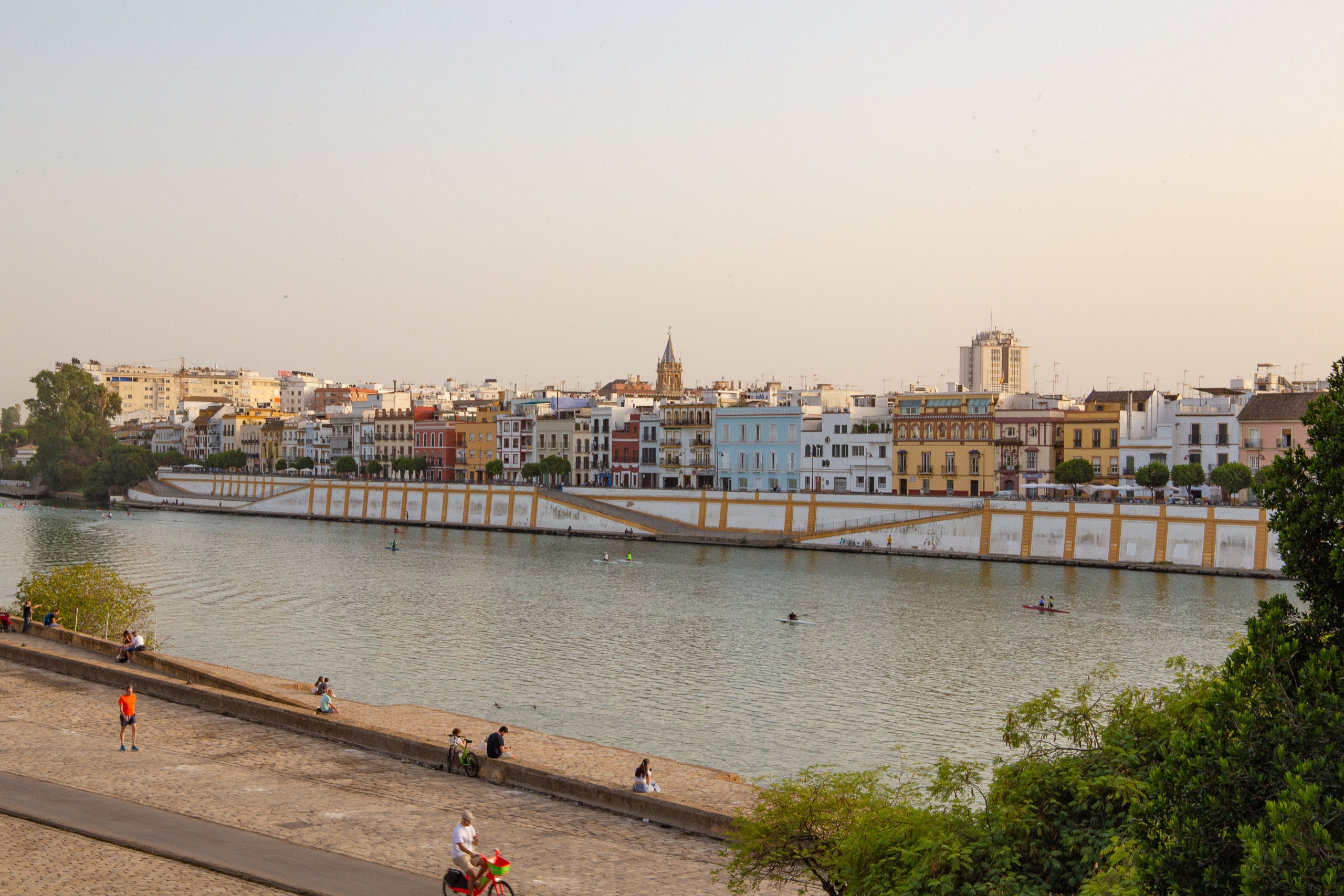 Riverside buildings in Seville with people walking and cycling on the path.