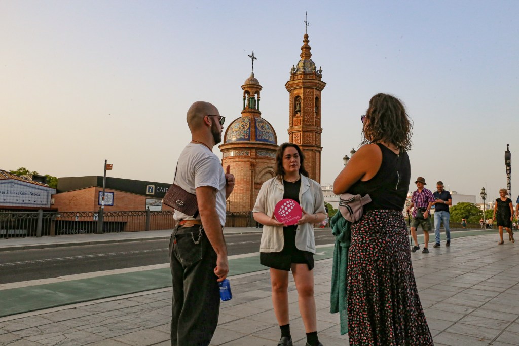 Three people talking near a domed building and tower at sunset.