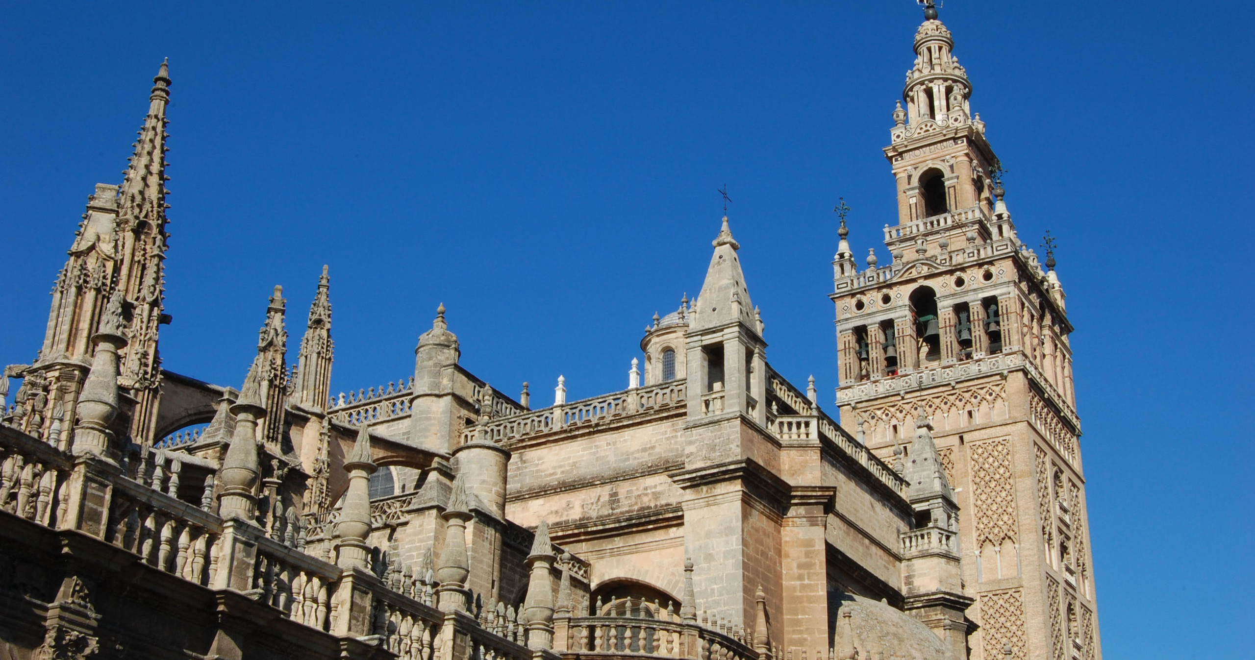 Gothic cathedral with ornate spires and a tall bell tower against a clear blue sky.