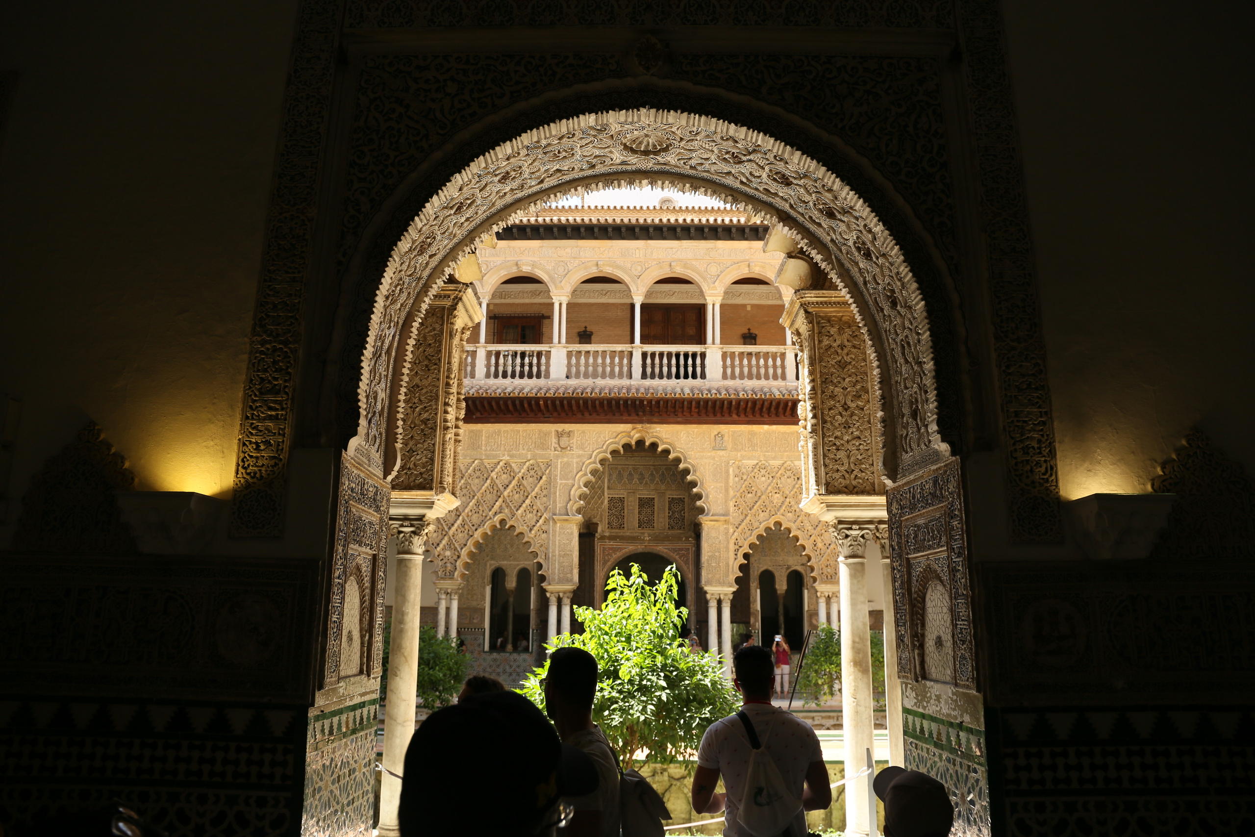 Ornate archway framing a courtyard with detailed architecture and a tree.