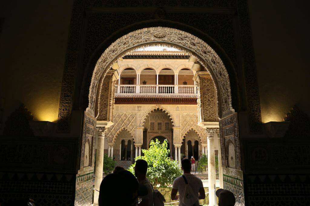 Ornate archway framing a courtyard with detailed architecture and a tree.