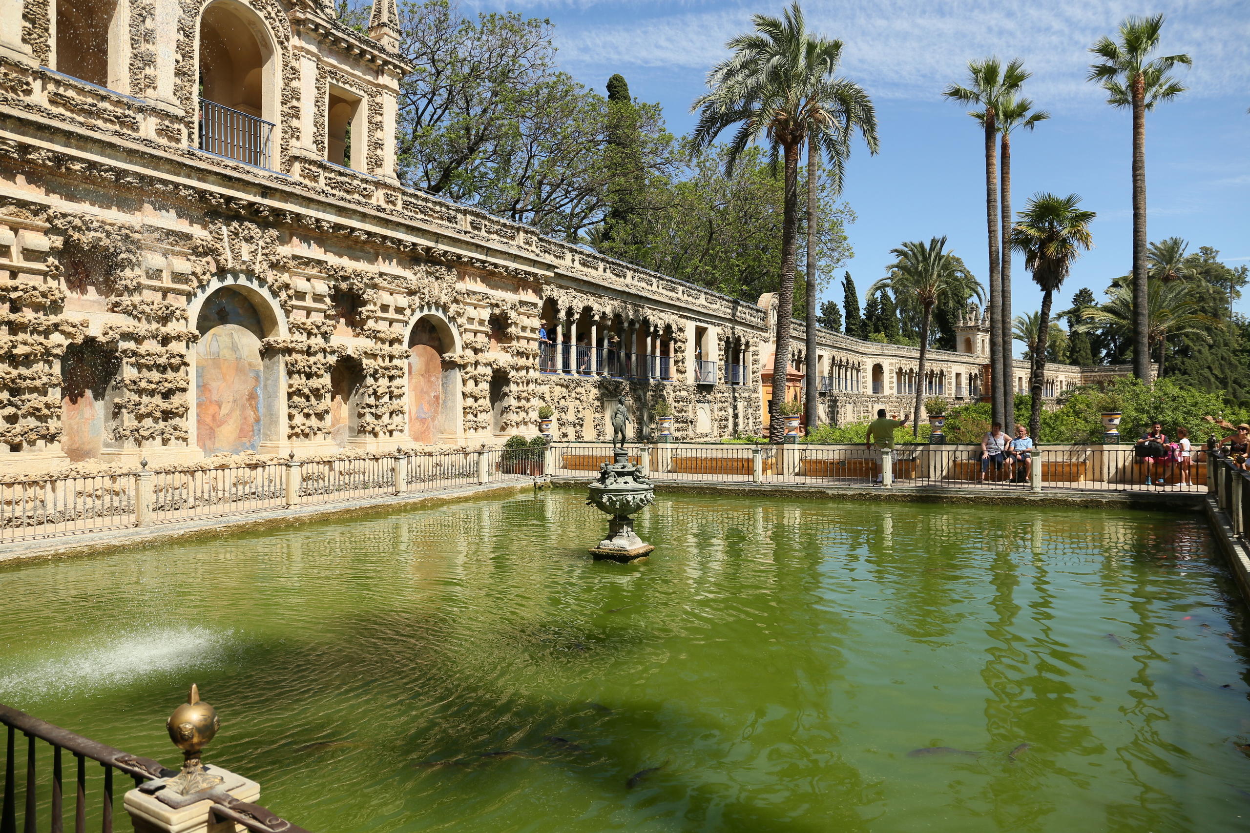 Historic palace with ornate walls and a green pond surrounded by palm trees.
