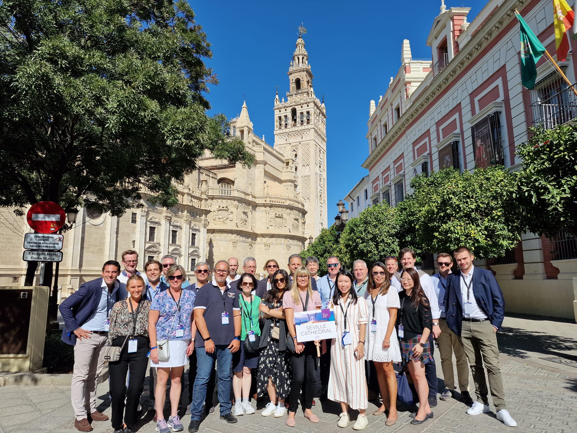 Group of people posing in front of a historic building on a sunny day.